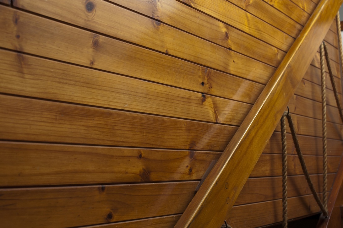 A close-up view of honey-toned wooden wall paneling with horizontal planks meeting at an angle, likely part of a ceiling or staircase detail. The wood features visible grain patterns and knots, showcasing natural material as an interior design element. The warm finish suggests a rustic or cabin-like interior aesthetic where wood serves as both structural and decorative element.